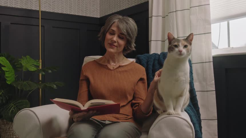 A woman is reading while she pets her cat