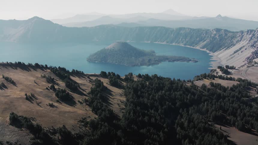 Aerial view of a deep blue lake surrounded by rocky mountains and dense forests