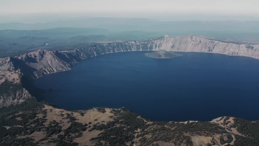 Aerial view of a crater lake with fog covering mountains in the horizon