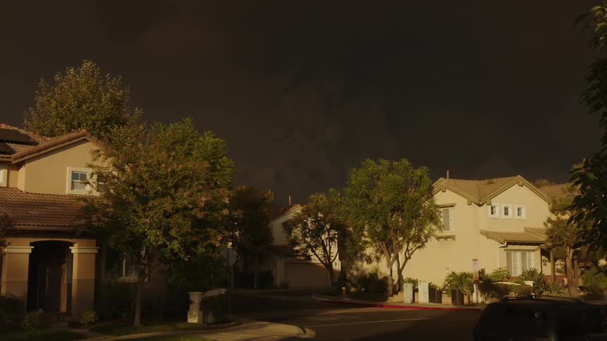 Truck travels in a neighborhood as sunlight shines upon the houses under a dark ominous sky