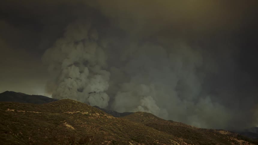 Dark thick smoke rises over the mountains and fills the air