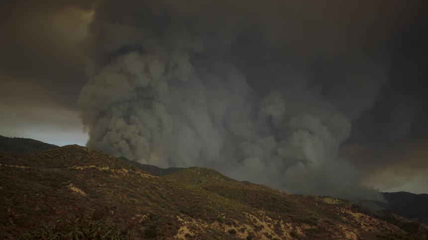 Dark thick smoke rises over the mountains and fills the air