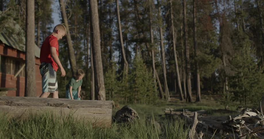 Two young boys stand outside a cabin throwing rocks
