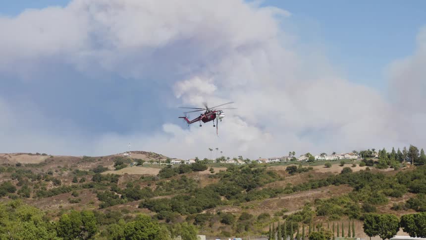 Aerial view of a rescue helicopter operating and descending in a mountainous area with sparse vegetation