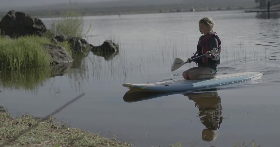 A woman rows on a surfboard towards the shore