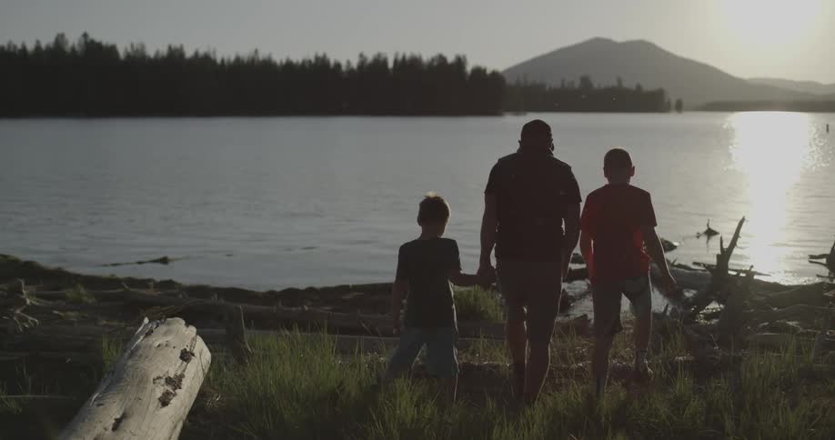 A man and two children walk towards a lake