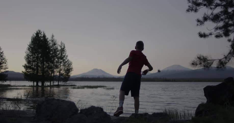 A boy throws a large rock in the lake