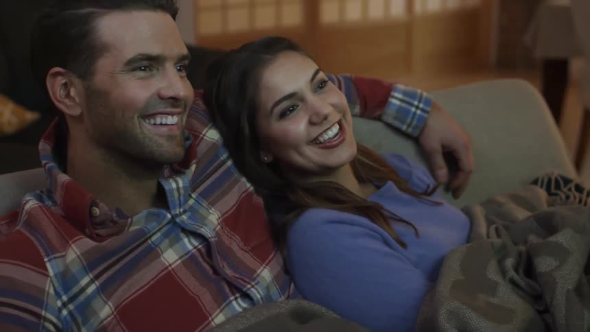 A man and woman are sitting close together on a couch watching tv