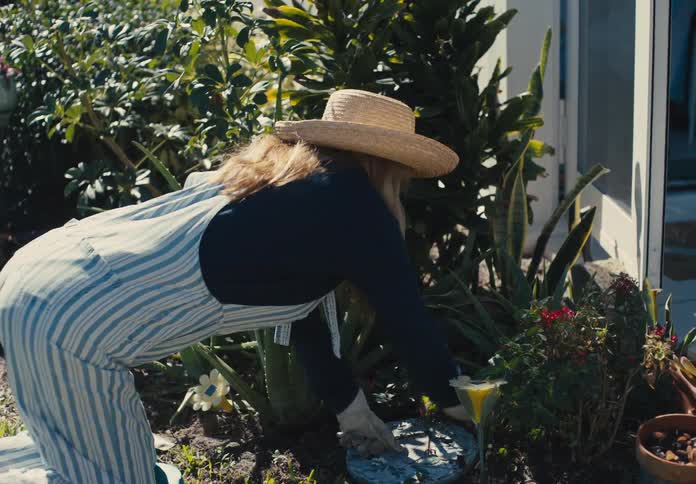 Woman balances on both knees and one hand while planting in the garden near her house