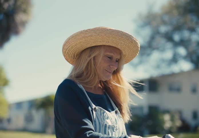 Blonde woman in sun hat outdoors in a garden holding a hose