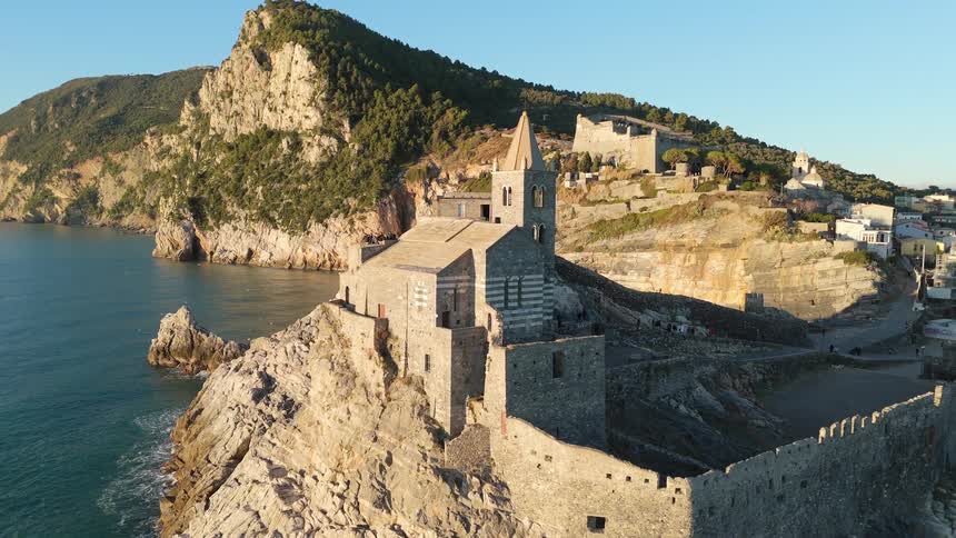 People stand on the roof of a historic castle set on a cliff near a coastal town on a summer day