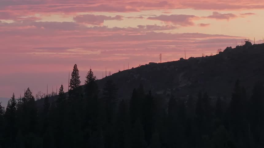 Aerial panorama of conifers surrounded by mountains against a reddish sky