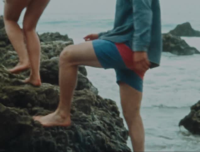 Man and his female friend climb a rocky shore barefoot on a misty day
