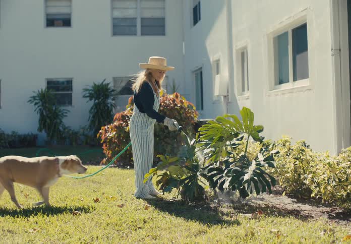 A dog walks up to a woman watering her plants