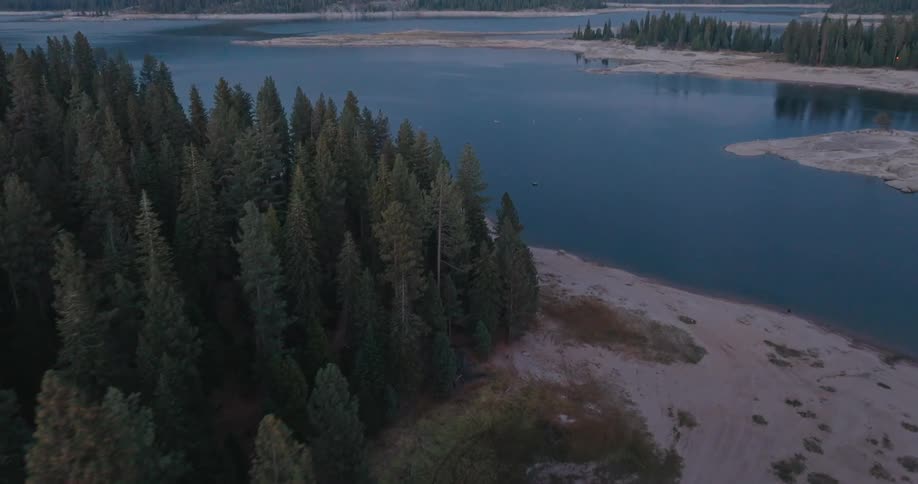 A calm lake stretches out between a dense forest and a sandy shoreline
