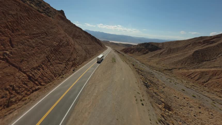 A bus is traveling along a winding road through a barren mountainous desert landscape under a clear blue sky