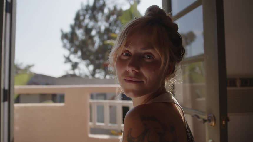 Portrait of a young blonde woman standing next to a window with a happy facial expression