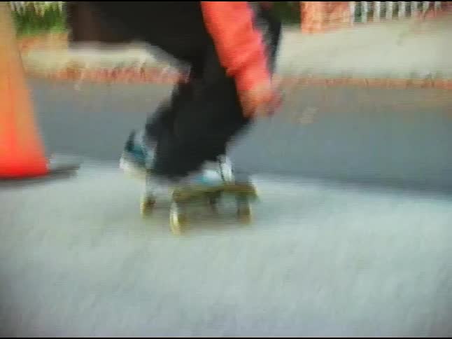 Curly haired boy doing a skateboard trick jumping over a cone