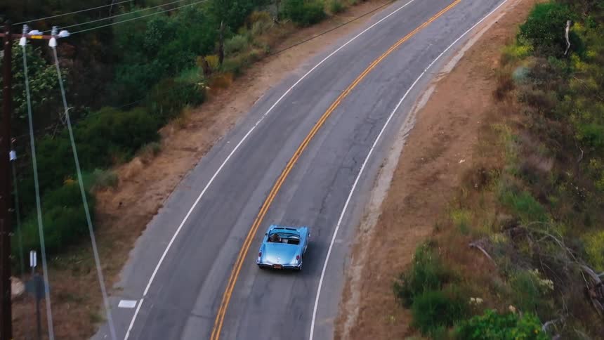 Aerial view of a classic blue convertible car traveling down a highway