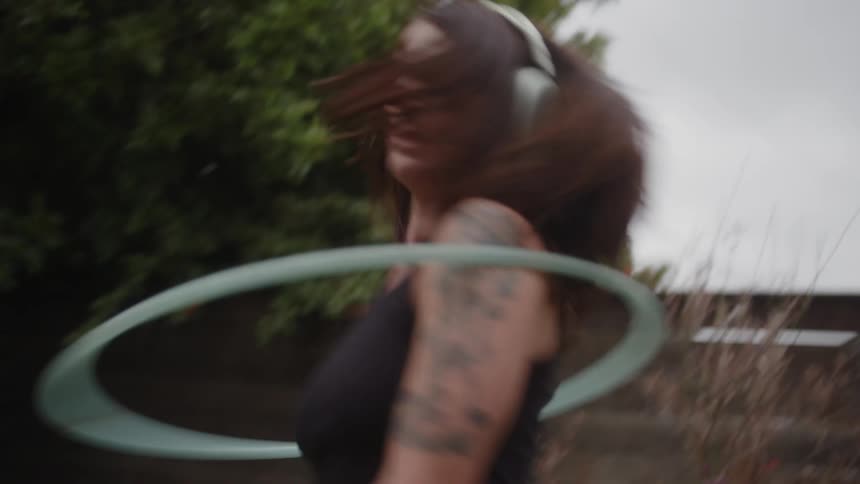 Woman with headphones dancing with a hula hoop in a garden