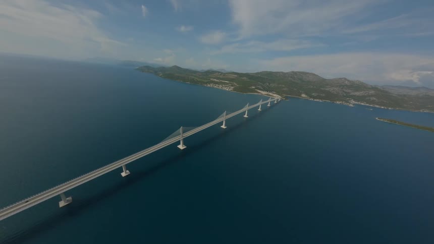 Aerial view of a long bridge over the ocean leading to a mountain in the background
