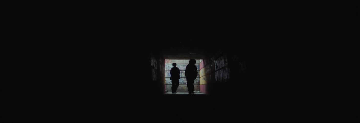 Silhouette of two people skateboarding through a dark tunnel