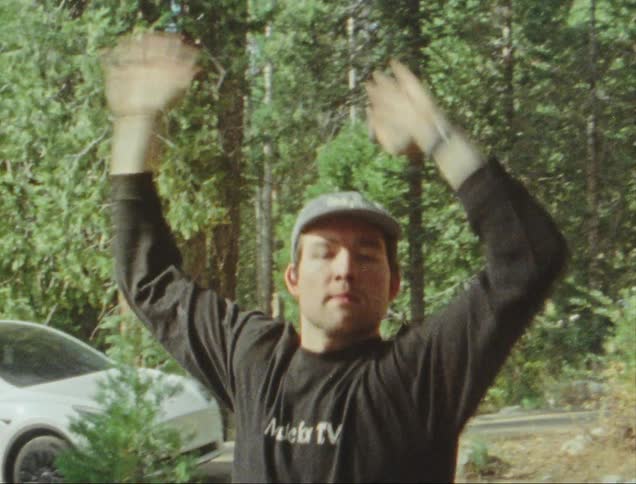Man in cap outdoors with forest in background dancing with arms up