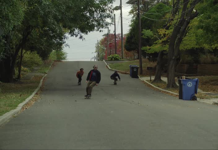 A teenager falls while skateboarding down the street