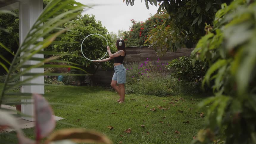 A teenage girl practices a hula hoop performance in her backyard