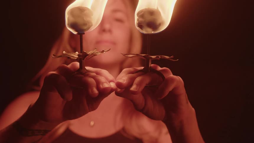 Woman holding two chalices with fire and raising her hands in a ceremony