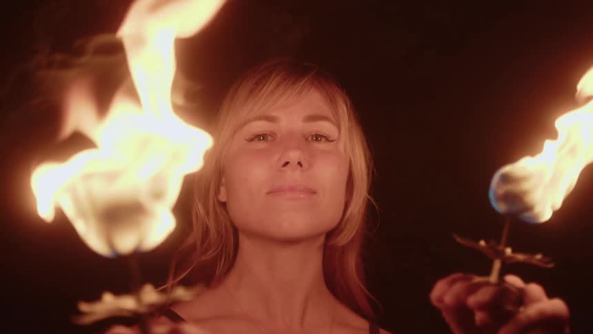Portrait of a blonde woman holding two chalices with fire in a ritual at night