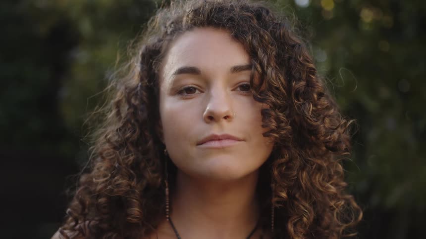 Portrait of a young woman with curly hair outdoors with a blurred greenish background
