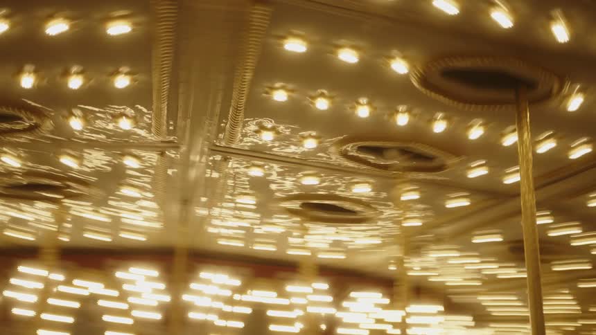 A carousel with brightly lit lights spins rapidly creating a blur of golden light and motion as the riders are whirled around