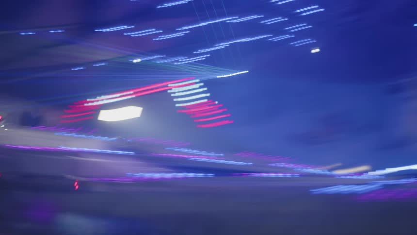People on a spinning ride at amusement park with moving neon lights