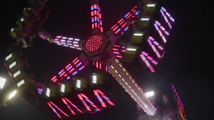 People with their legs suspended from a thrill ride at an amusement park at night