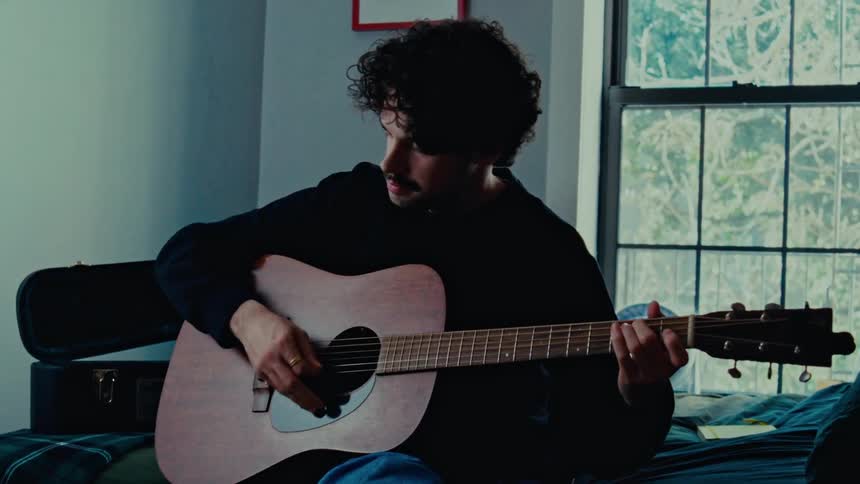 Man sitting inside a room playing an acoustic guitar