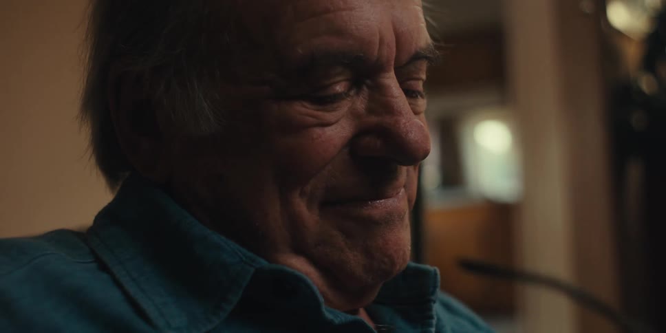Elderly man sitting at home smiles before putting his eyeglasses on