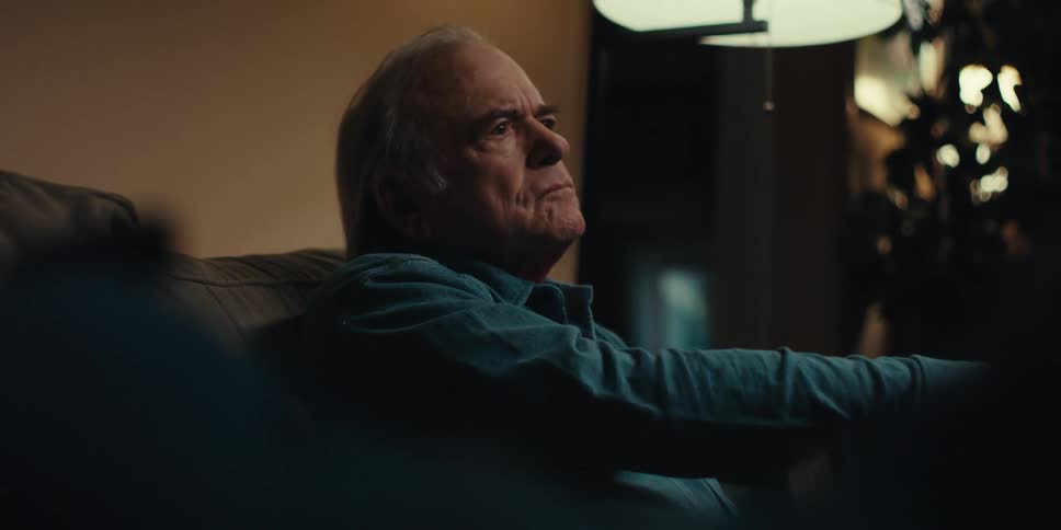 Elderly man sitting in an armchair looking forward and taking off his glasses
