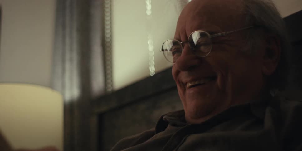 Elderly man sitting in bed laughs while reading a book