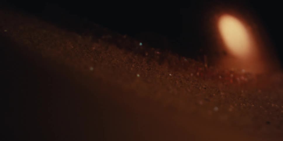 The flame of a candle flickers casting a warm glow on the rough textured surface of its wax