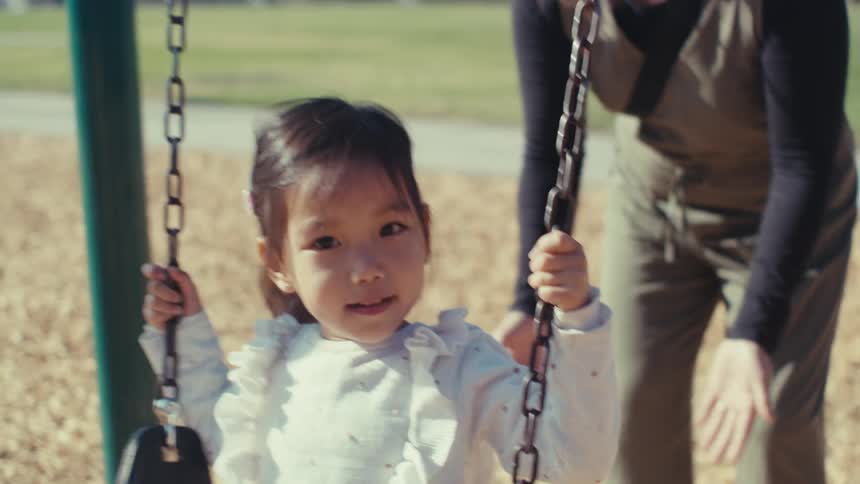 Mother pushing her little daughter on a swing outdoors