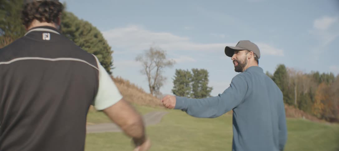 A couple of men walk on a golf course fist bumping each other in celebration