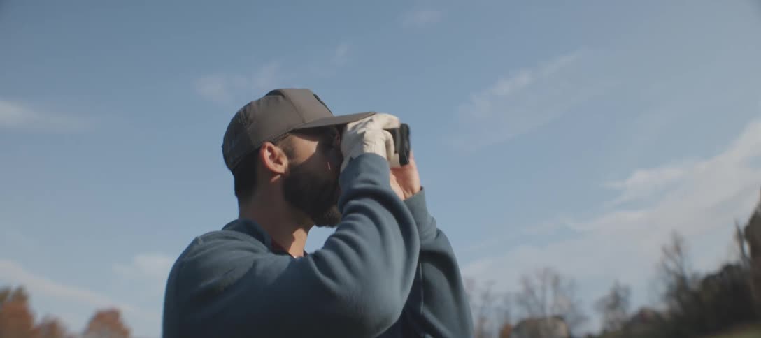 Man in a field looking through binoculars