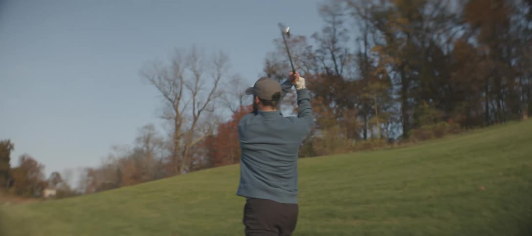 A male golfer swings a club on a golf course on an autumn day