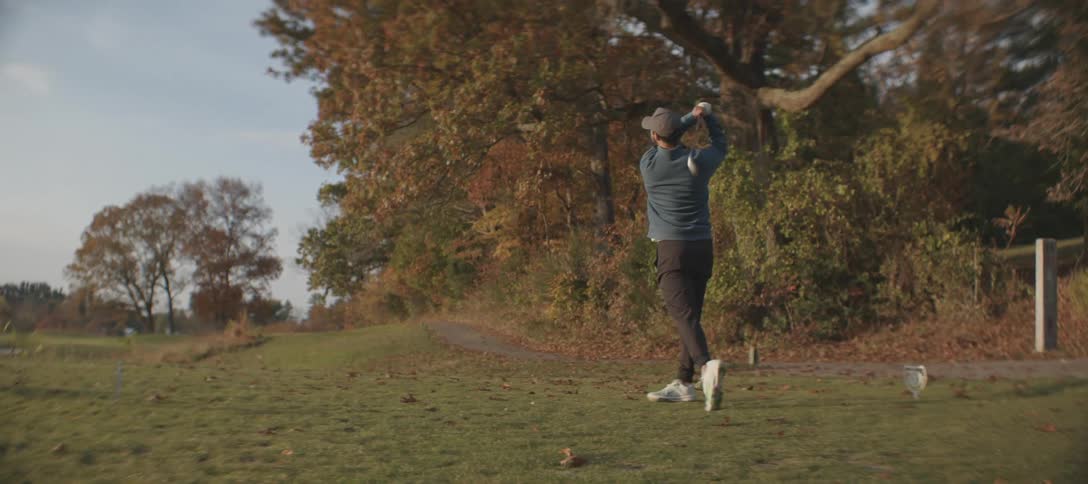 A male golfer swings a club on a golf course on a mostly sunny autumn day