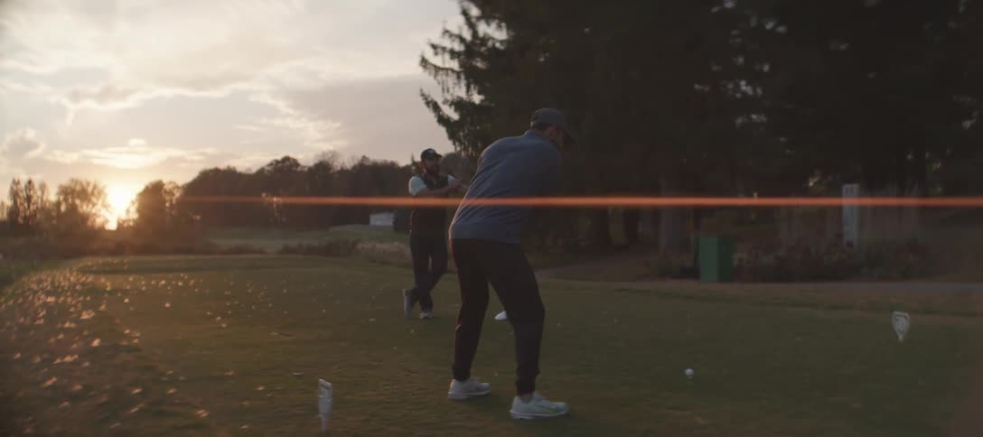 Two men are playing golf at sunrise using drivers