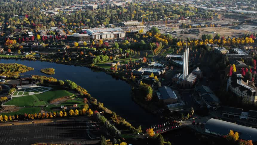 An aerial view of a city with a river winding through it surrounded by lush green areas and buildings of various sizes and styles