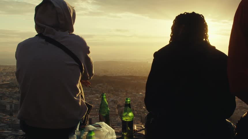 Friends drink while sitting at a high spot and looking towards the red tinted horizon