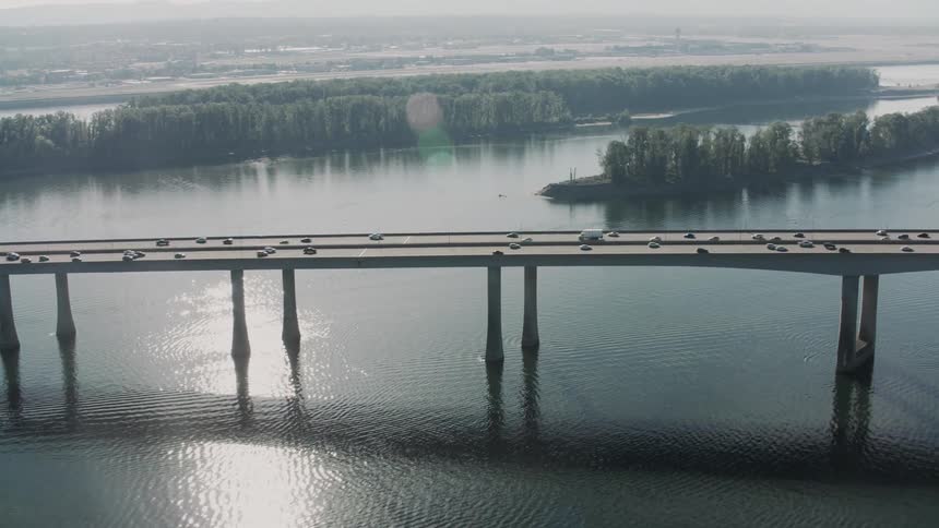 An aerial view of a long bridge spanning a wide river with numerous vehicles traveling across it