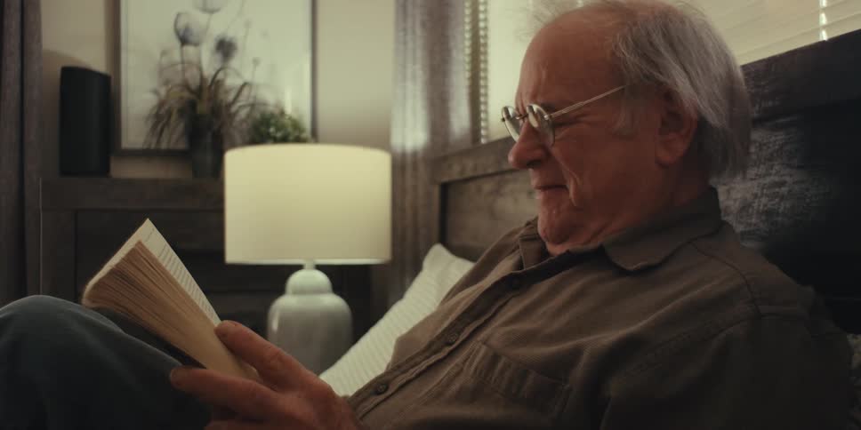 Man lying in bed with glasses reading a book